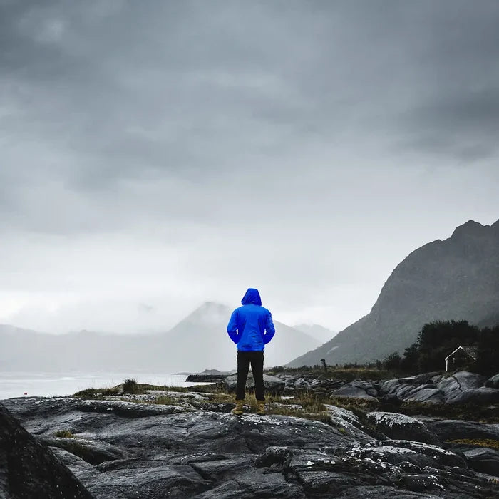 Man wearing a Sub Zero lightweight waterproof jacket in blue whilst standing by a lakeside in rainy weather