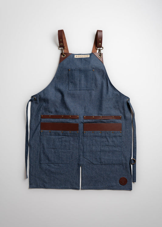Denim apron with leather straps and pockets, featuring brass rivets, displayed against a plain background for a rustic look.