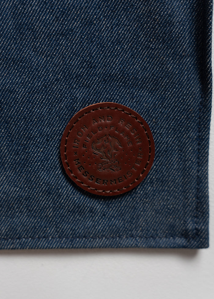 Denim fabric with a brown leather patch embossed with "Iron and Resin" and "Messermeister" logos, featuring a flame design.