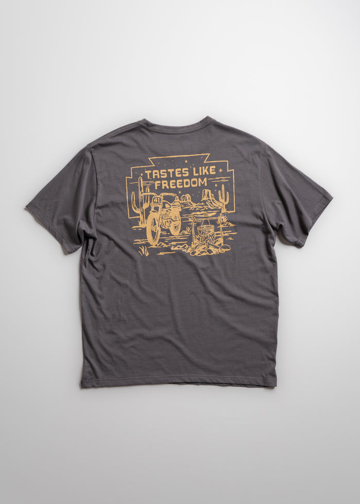Gray T-shirt with "Tastes Like Freedom" and desert scene printed in yellow on the back, featuring cacti and a motorcycle.