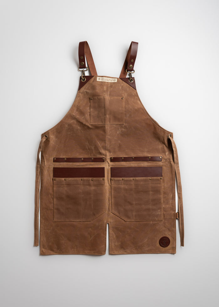 Brown leather apron with adjustable straps, multiple pockets, and a logo patch, laid flat on a white background.
