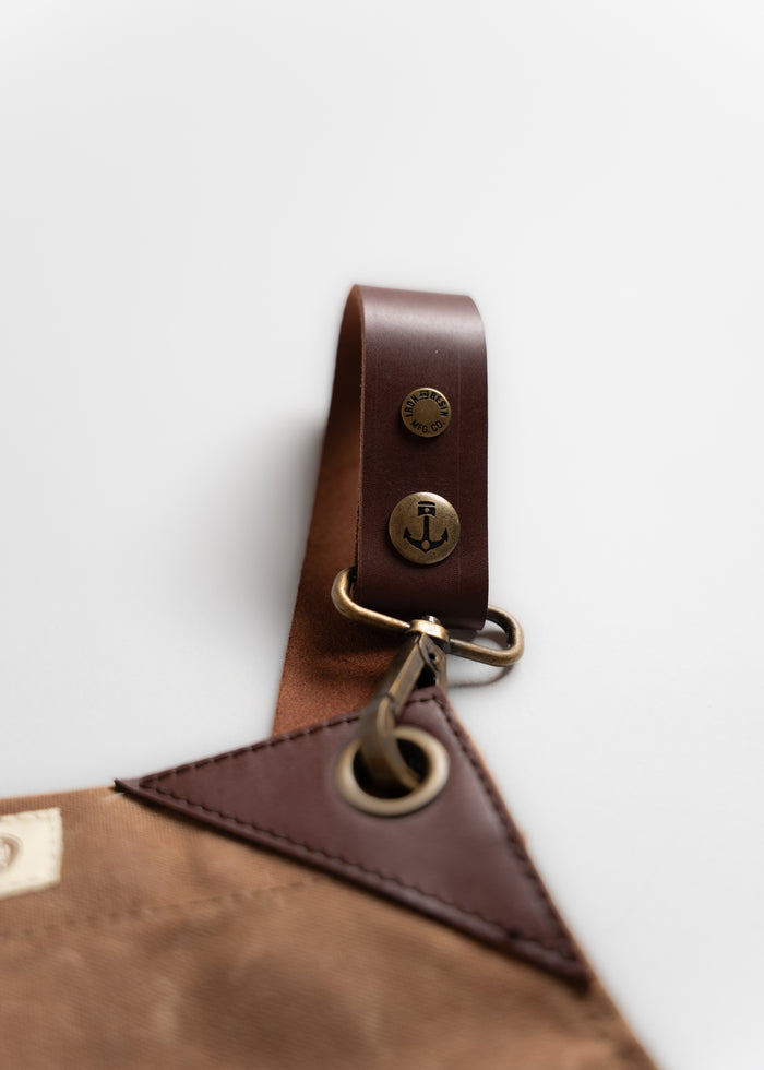 Brown leather strap with brass anchor rivets attached to a canvas bag corner, showcasing craftsmanship and durability.