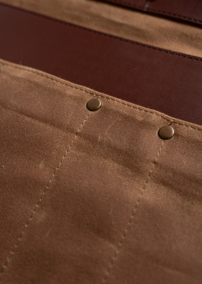 Close-up of brown canvas fabric with two metal rivets, showing texture and stitching details.