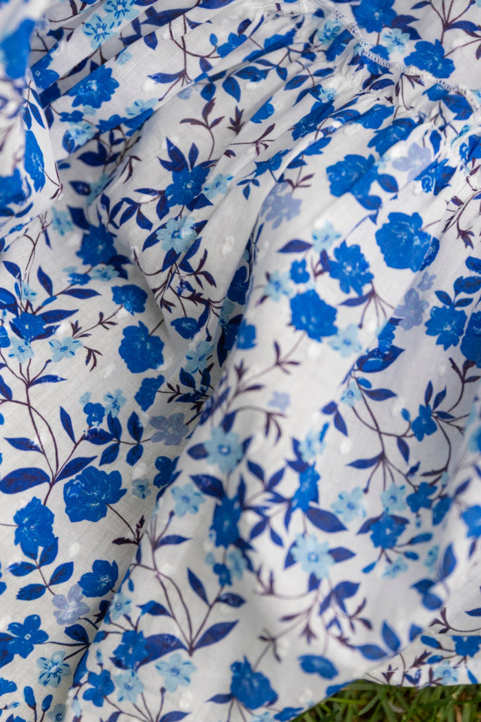 Close-up of the Mini Madeline Dress in Ditsy Cobalt Floral by Ivy City Co, showing white fabric with cobalt blue floral print and dark stems, draped in soft folds—perfect for a Mom and Me matching look. Grass peeks at the bottom edge.