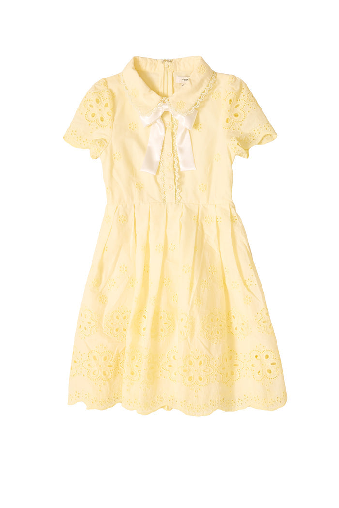The Mini Penny Dress in Butter Yellow Eyelet by Ivy City Co features floral embroidery, a peter pan collar, and a white satin bow. With a fitted waist and flared pleated skirt, it’s perfect for matching mama and mini moments.