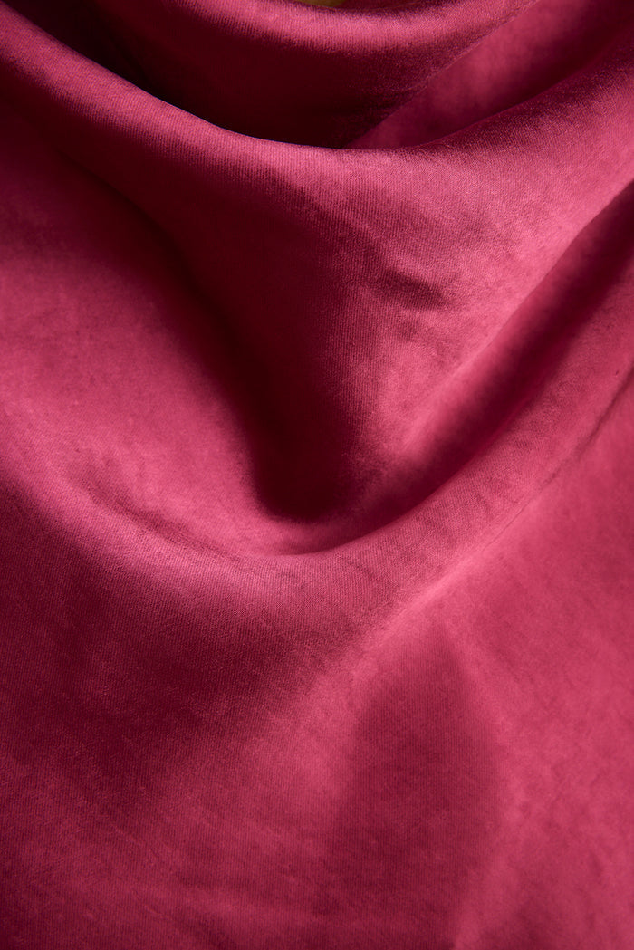 Close-up of draped fuschia satin showing the cowl back on this maxi dress.