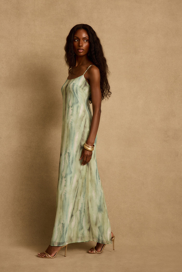 Side profile of the Nerissa sage watercolor chiffon maxi dress with gold heels and bangles.