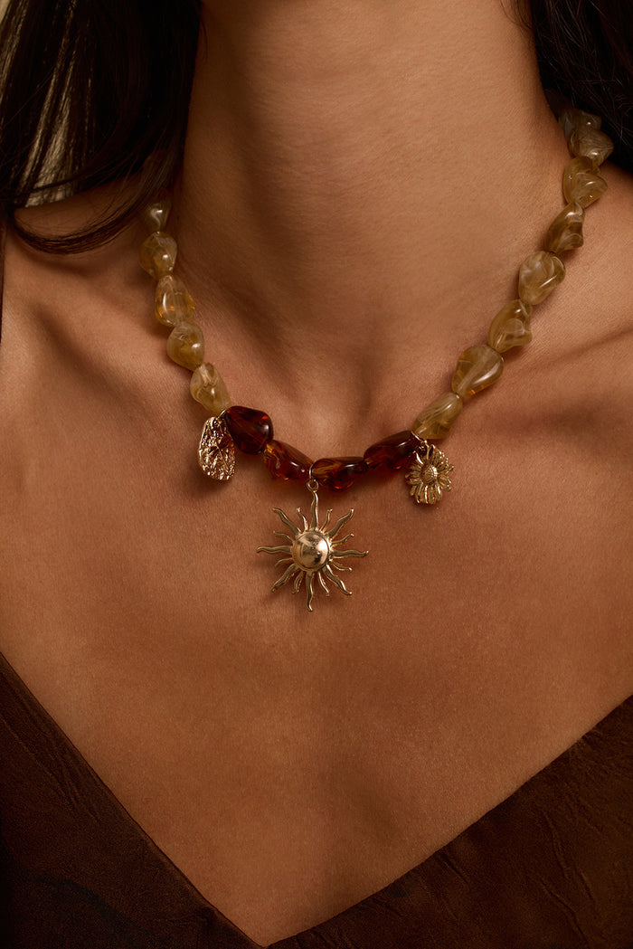 Close-up of gold sun charm necklace with amber and honey stones worn at the collarbone.