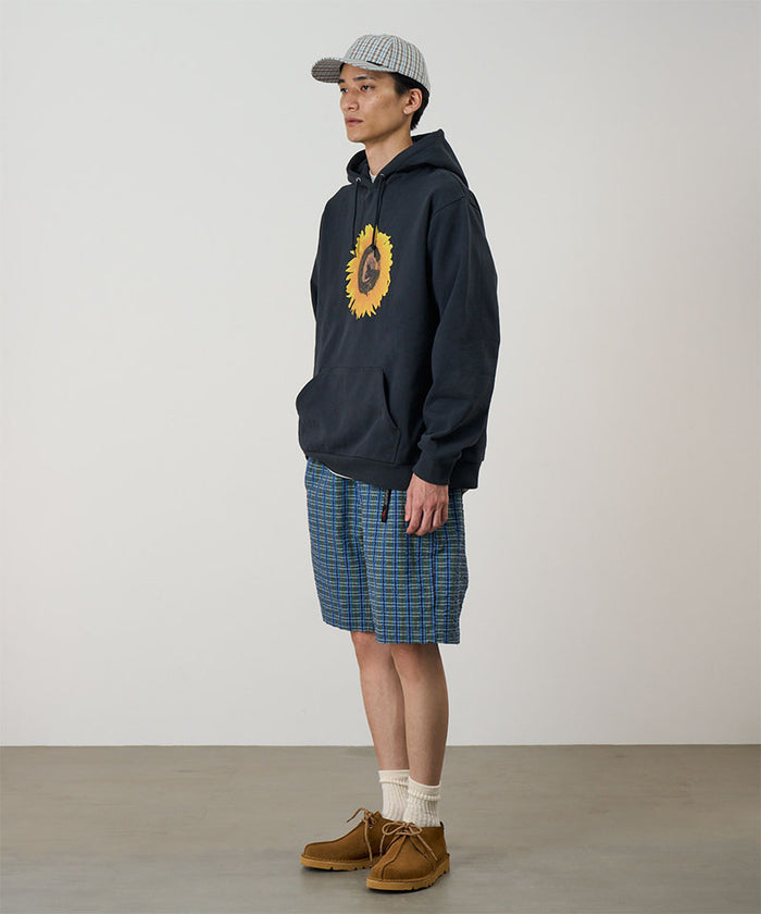 Model wearing a blue multistripe Gramicci Gramicci O.G. G-Short Seersucker Plaid with grey and green graphic and navy hoodie on a light-tone background.