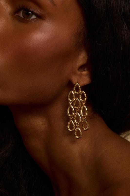 Close-up of a hammered gold chandelier statement earring worn against the neck.