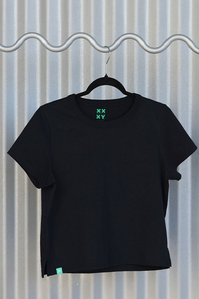 Black t-shirt with green logo on a hanger against a corrugated metal background || black