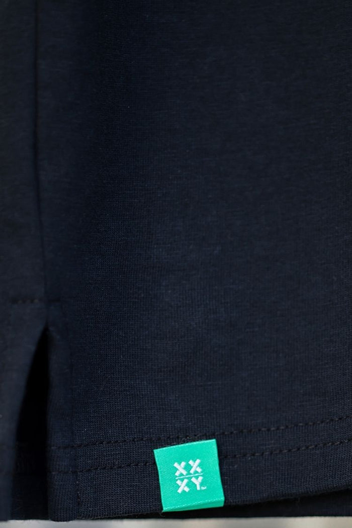 Close-up of a black fabric with a green label featuring 'XXY' branding. || black