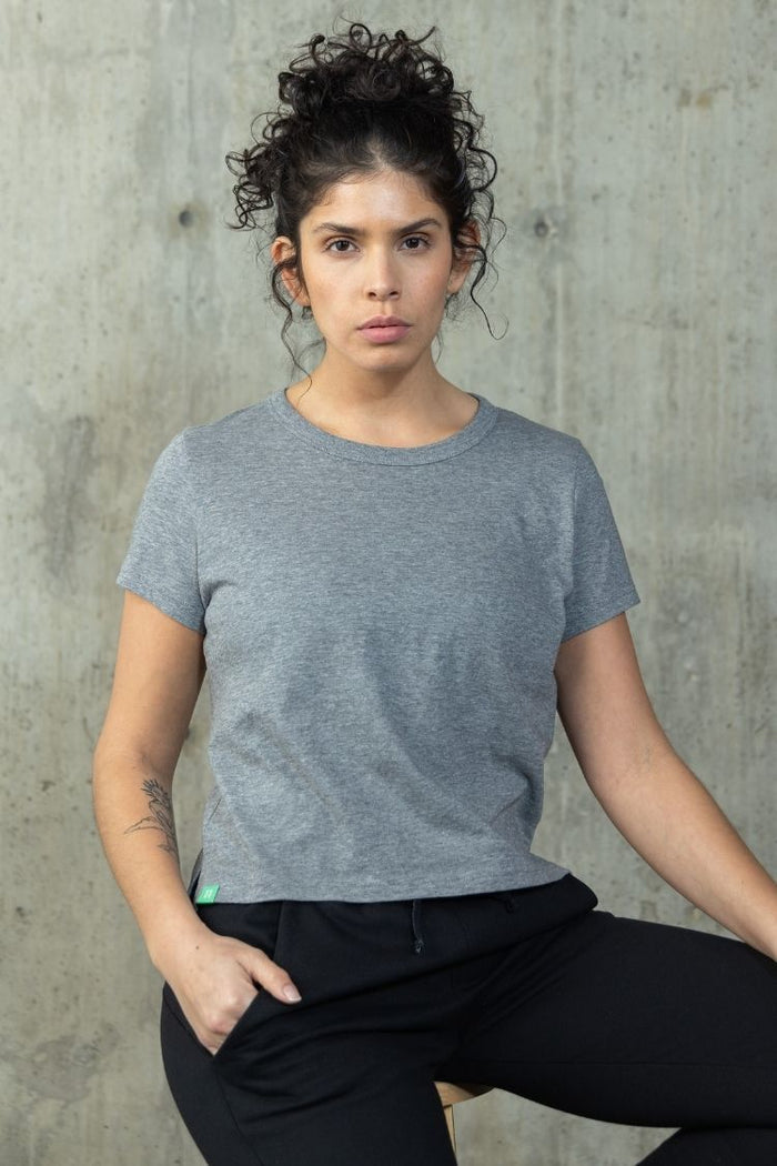Woman wearing a gray t-shirt and black pants against a concrete wall. || heather gray
