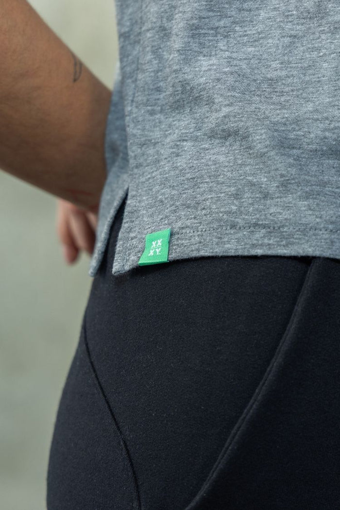 Gray shirt with a green tag worn by a person, on a neutral background || heather gray