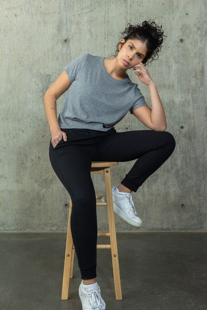 Woman sitting on a stool against a concrete wall wearing a gray t-shirt and black leggings. || heather gray