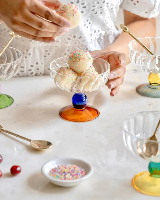 Clear glass dessert bowl on colorful pedestal stand, with ice cream and sprinkles