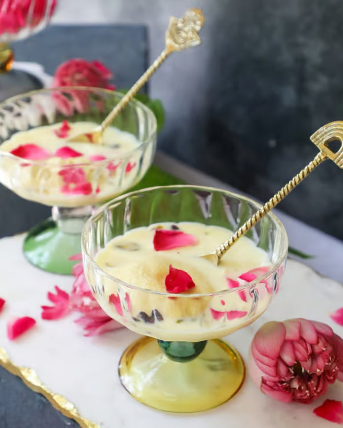 Glass dessert bowl on gold pedestal stand with white dessert and pink flower petals