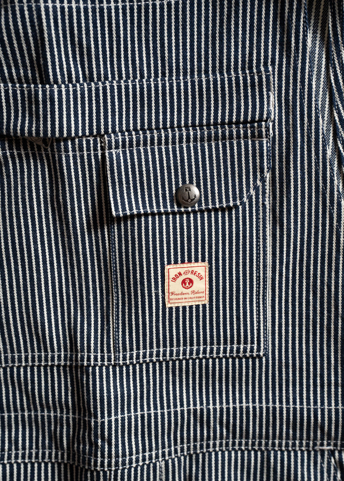 Close-up of blue and white striped fabric with a pocket, button, and a red "Iron and Resin" label, emphasizing texture.