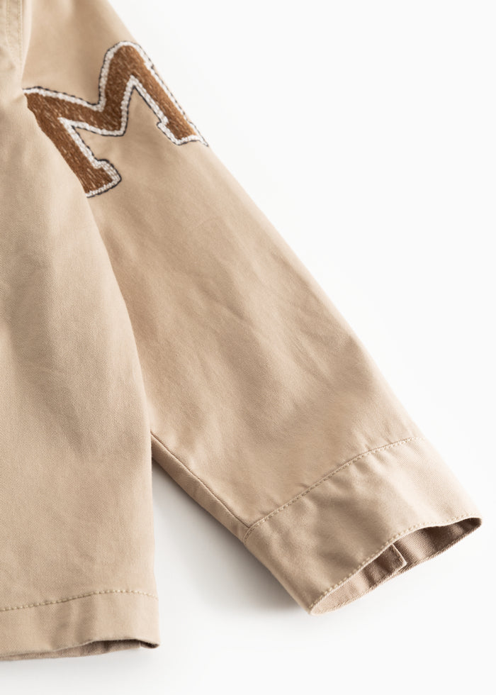 Beige jacket sleeve with embroidered label patch on the shoulder