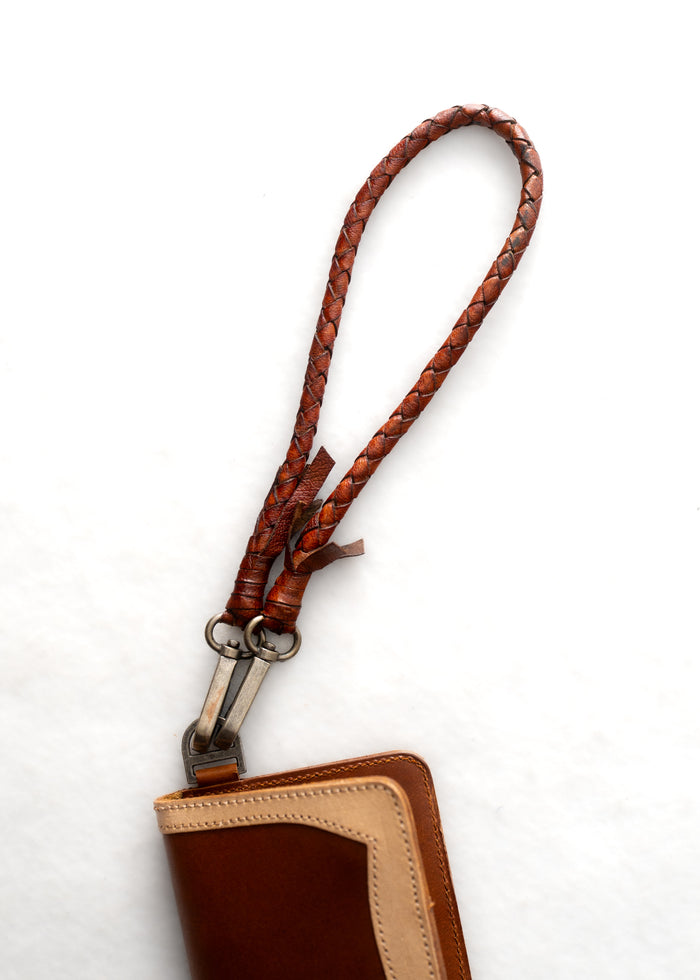 Brown leather wallet with braided strap against a white background, showcasing craftsmanship and style.